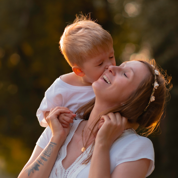 Kleiner Sohn küsst Mama auf einer Wiese im Park – Golden Hour in Berlin