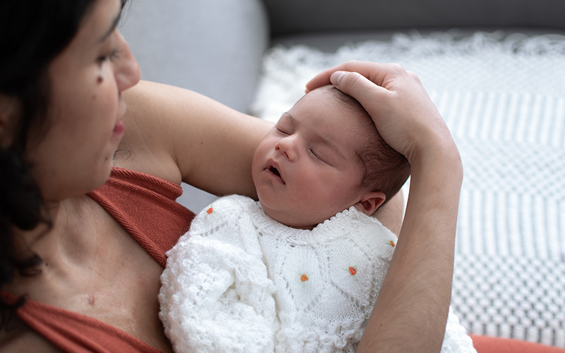 Mama hält ihr Neugeborenes im Arm und schaut liebevoll darauf