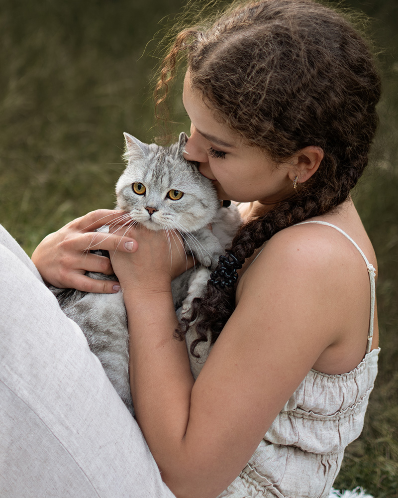 Junge Frau sitzt entspannt auf einer Decke im Gras bei einem Fotoshooting mit Katze