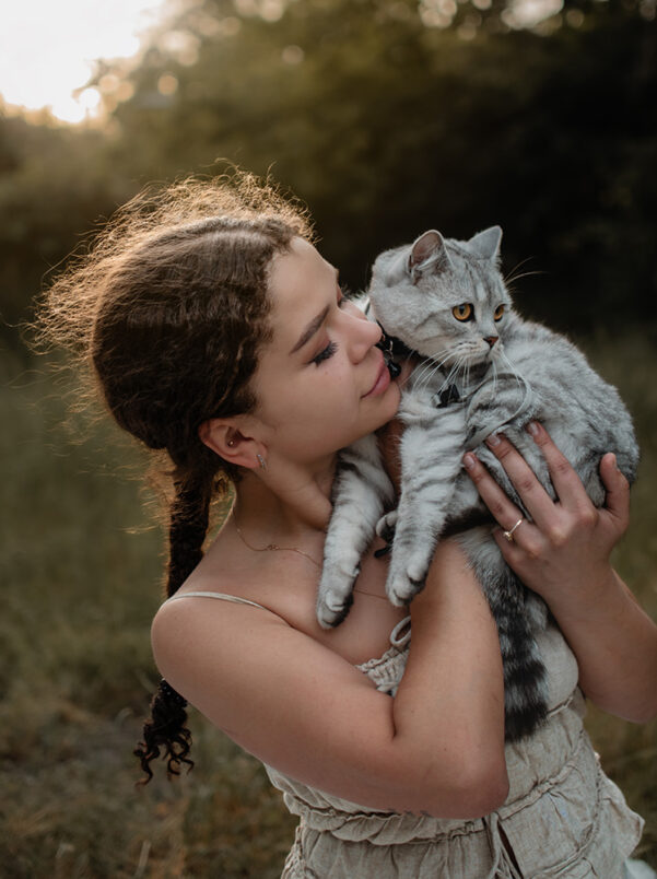 Junge Frau hält ihre Katze liebevoll im Arm bei einem Fotoshooting in der Natur