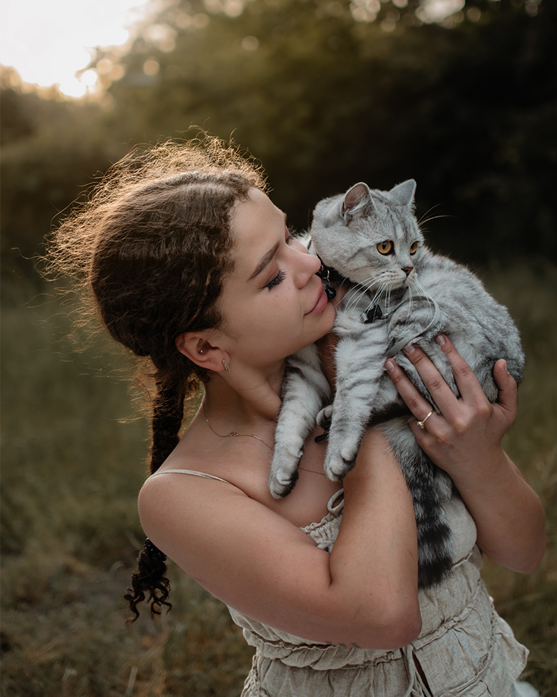 Junge Frau hält ihre Katze liebevoll im Arm bei einem Fotoshooting in der Natur