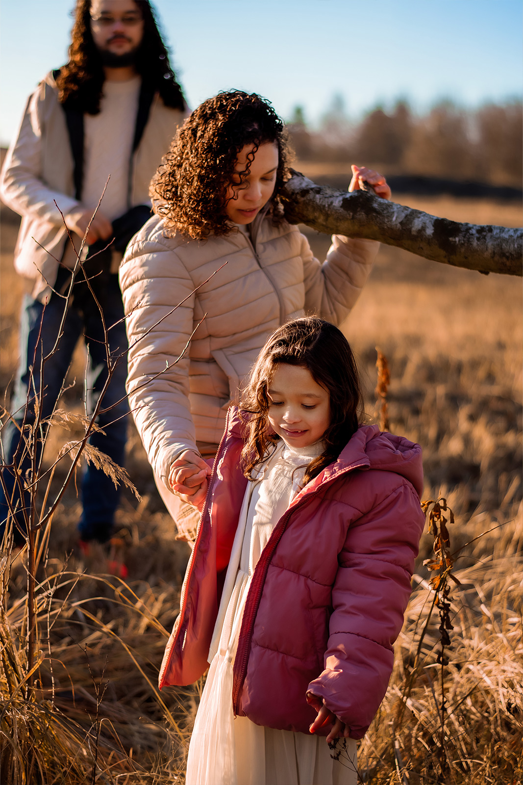 Eine Familie geht gemeinsam durch eine winterliche Naturlandschaft im Sonnenlicht, während die Mutter ihre Tochter an der Hand hält. Authentische Familienfotografie in Deutschland.