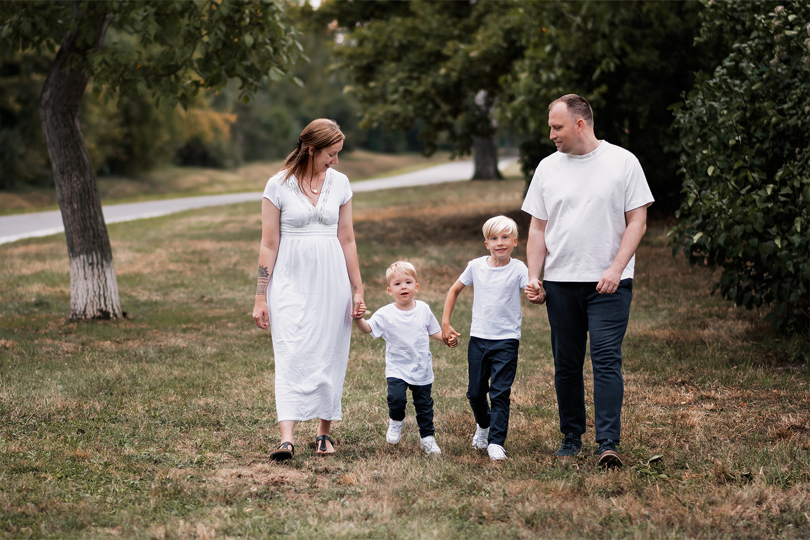 Eine vierköpfige Familie geht Hand in Hand über eine grüne Wiese im Park spazieren. Authentische Familienfotografie im Freien in Deutschland.