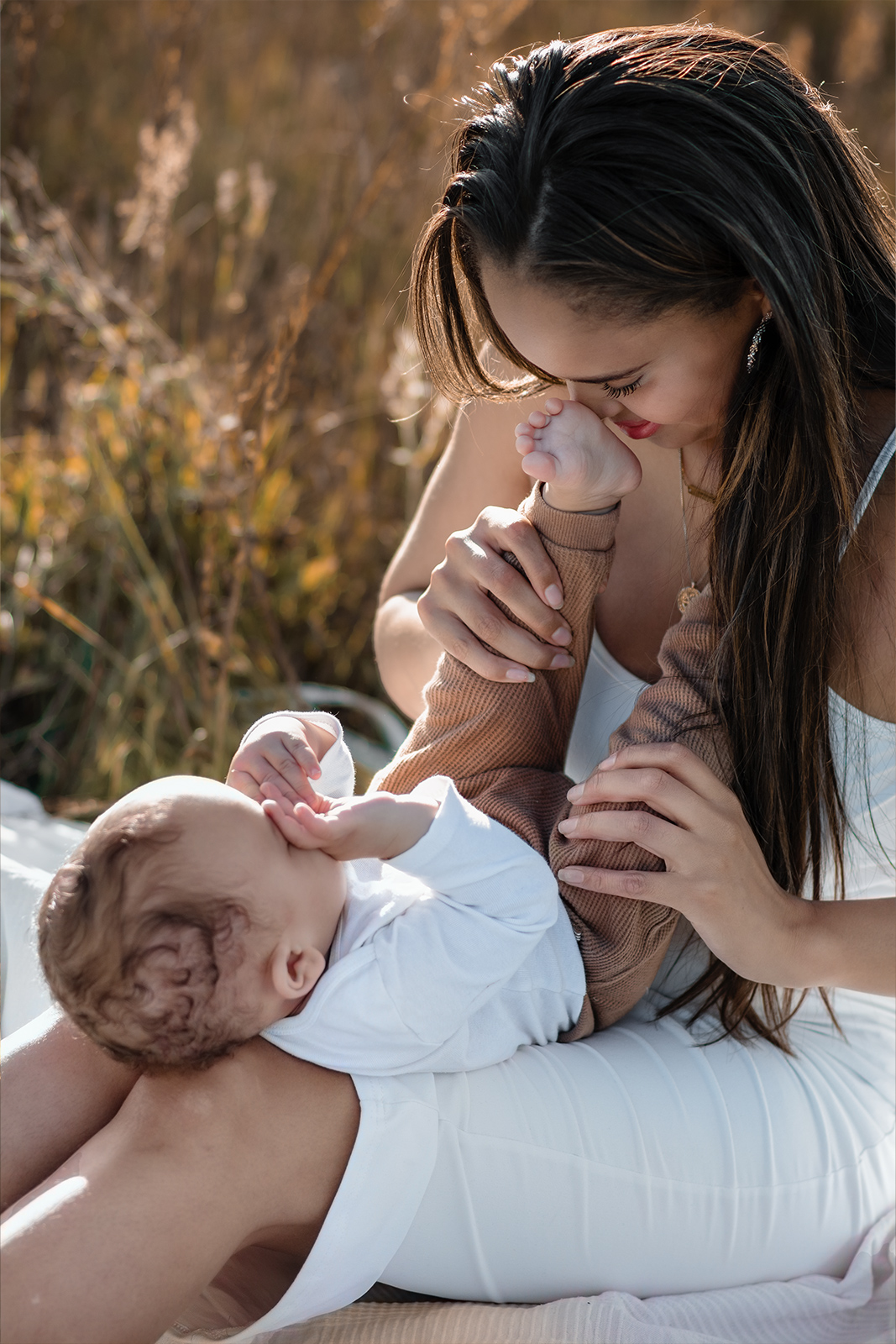 ine liebevolle Mutter küsst die Fäßchen ihres Babies während eines Picknicks im Freien. Sinnliche Familienfotografie in der Natur in Deutschland.
