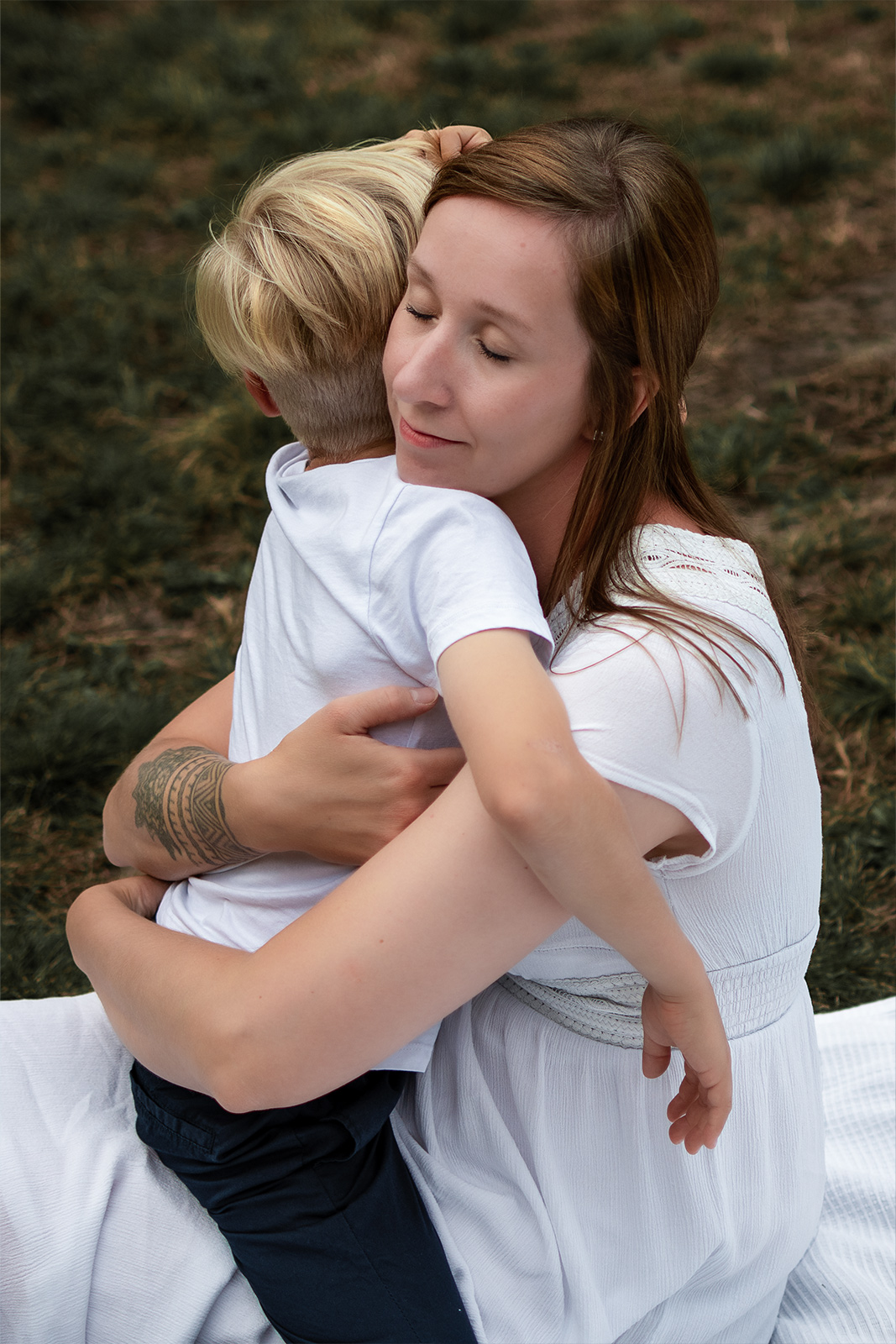 Eine Mutter hält ihren blonden Sohn innig im Arm und schließt liebevoll die Augen bei einem Familien-Fotoshooting im Freien in Deutschland.
