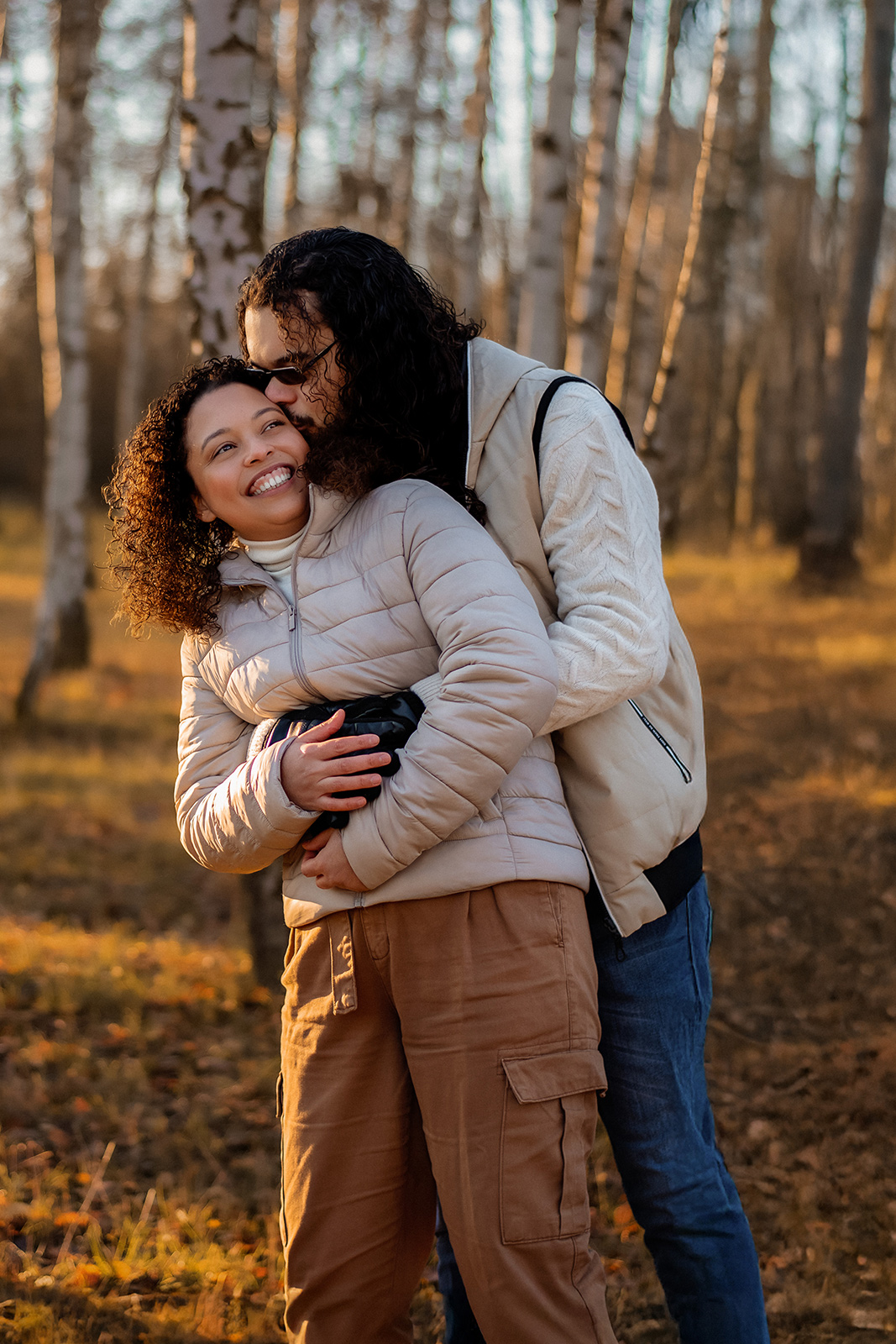 Ein glückliches Paar umarmt sich liebevoll im sonnigen Wald bei einem Fotoshooting im Freien. Romantische Familienfotografie in Deutschland.