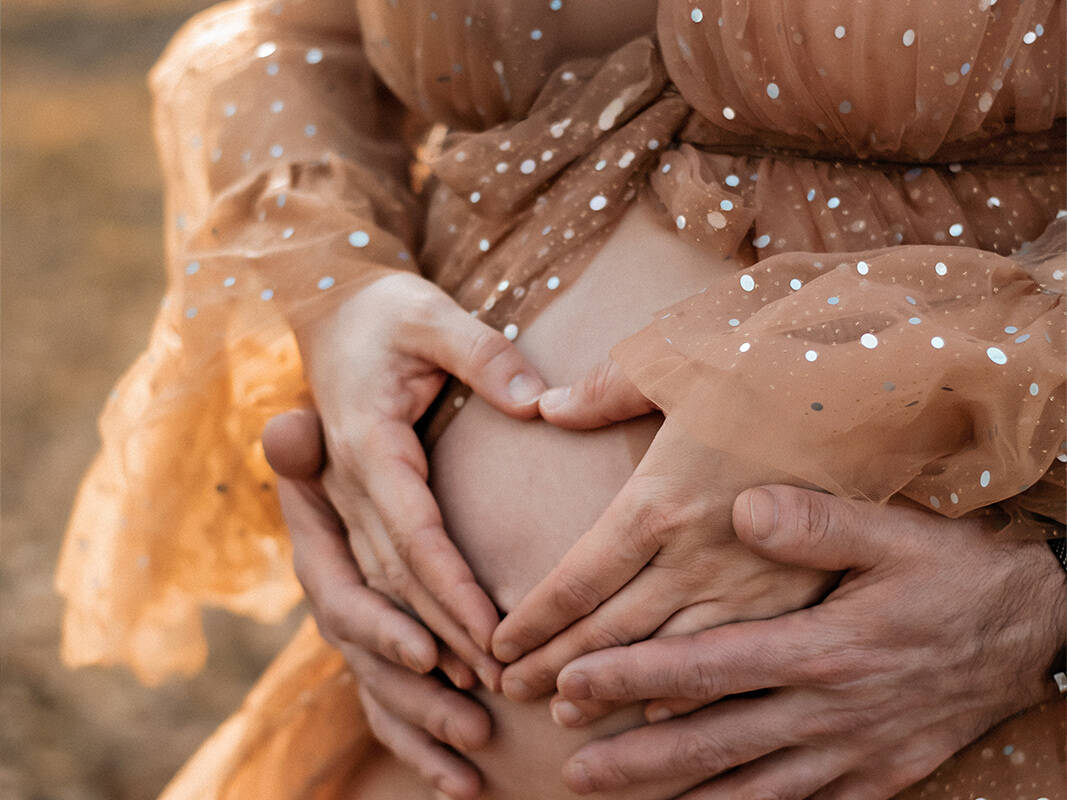 Nahaufnahme eines Babybauchs in einem glitter Tüllkleid, umrahmt von den Händen der Eltern, die ein Herz formen. Detailreiche Schwangerschaftsfotografie in Deutschland.